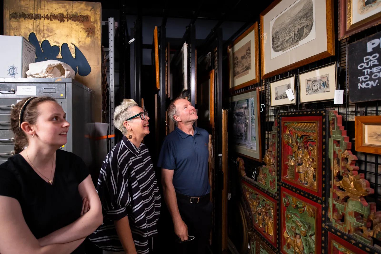 Behind-the-scenes tour of a museum's art collection at Sovereign Hill, with participants looking at various framed pieces stored on movable racks, including historical prints and intricate carvings.