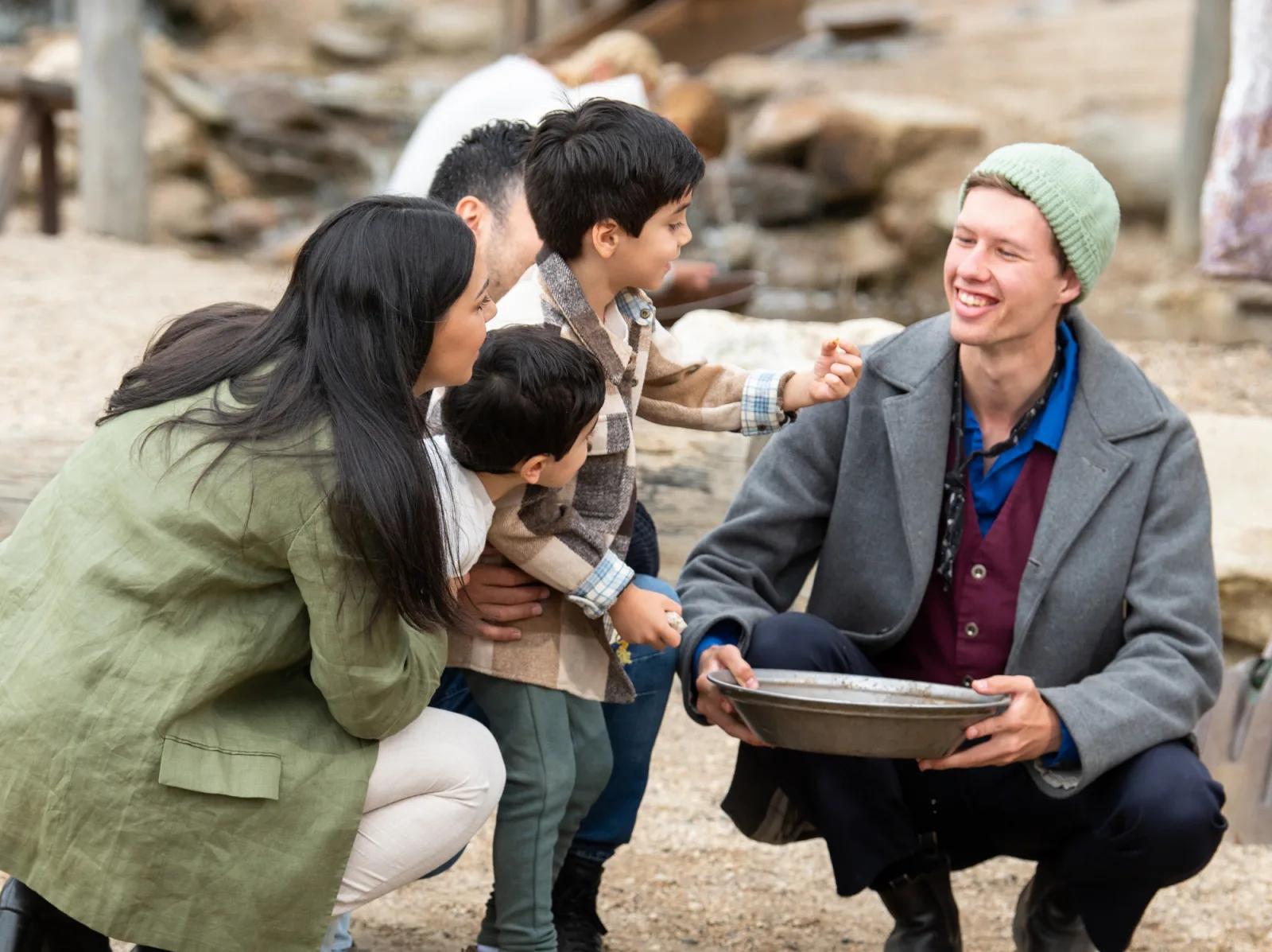 Visitor experience at Sovereign Hill's gold rush attraction, with a costumed interpreter showing gold panning techniques to a family.