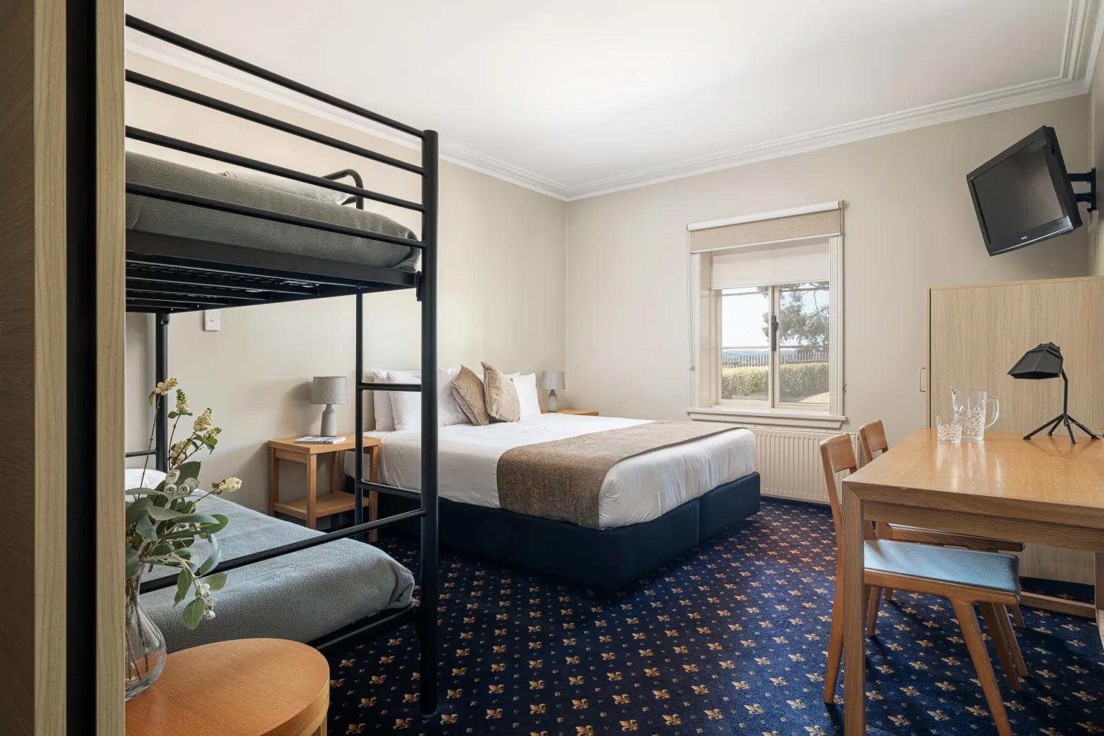 Sovereign Hill Hotel family room with a bunk bed, a double bed, a dining table with chairs, and a wall-mounted TV, featuring a dark patterned carpet.