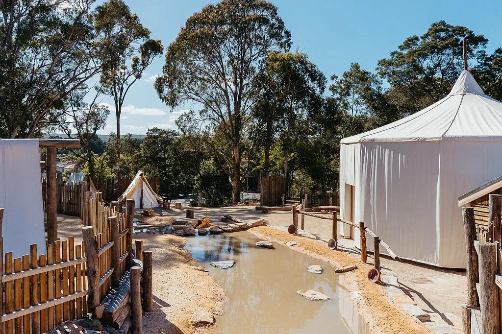 White tents, wooden walkways, and shallow pool surrounded by trees depicting Chinese Protectorate Camp gold panning zone