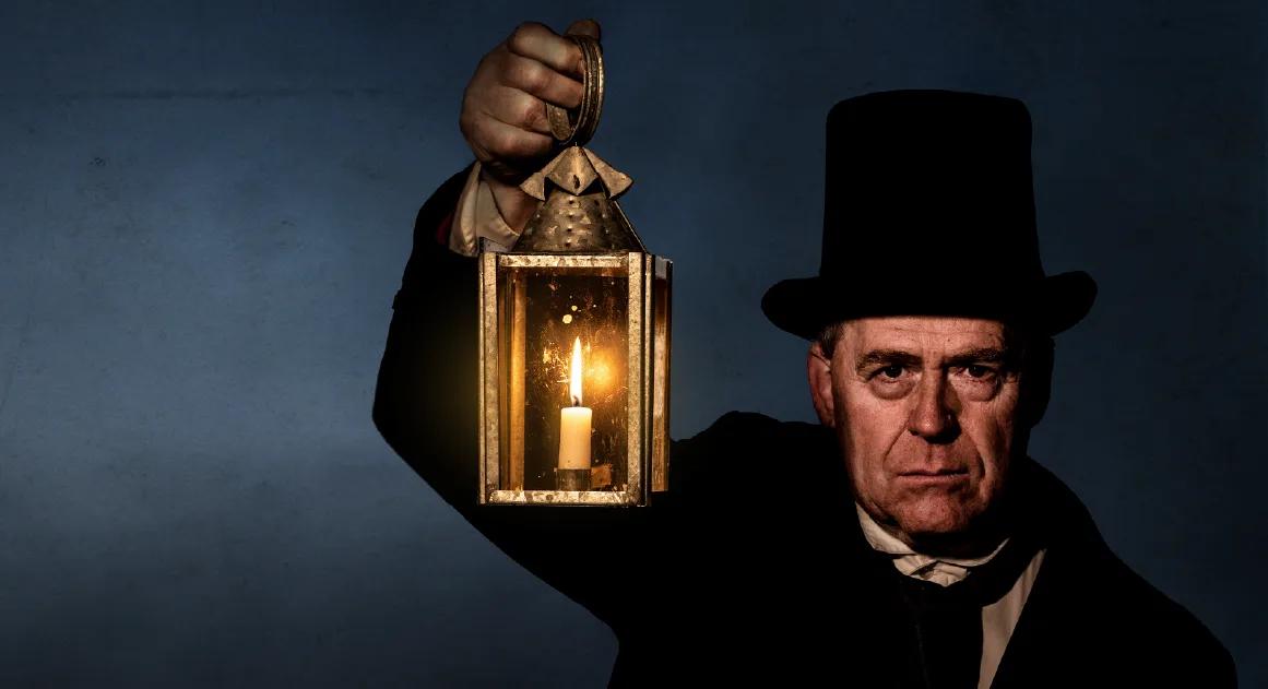 Costumed heritage actor holding a candle lantern in the dark, representing 19th-century life, from Australia’s most visited outdoor museum and heritage attraction.