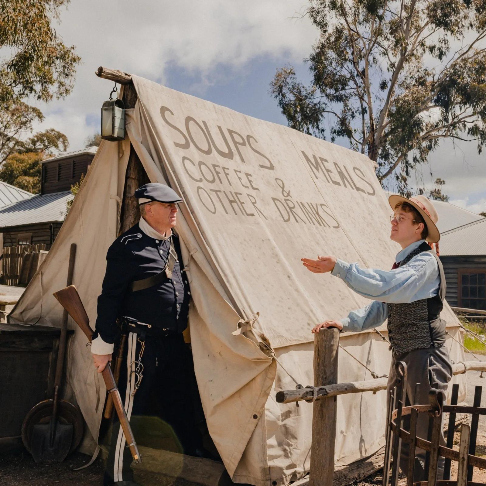 Gold rush era tent café sign offering soups, meals, coffee and drinks with reenactors interacting, from Australia’s most visited outdoor museum and heritage attraction.