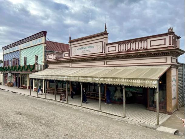 The historic Criterion Store stands prominently on the main street of Sovereign Hill, its ornate facade and striped awning evoking 1850s Ballarat. Visitors browse under the covered verandah, with neighbouring buildings including the United States Hotel and Victoria Theatre, completing the immersive gold rush streetscape at Sovereign Hill.