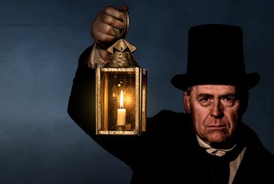Costumed heritage actor holding a candle lantern in the dark, representing 19th-century life, from Australia’s most visited outdoor museum and heritage attraction.